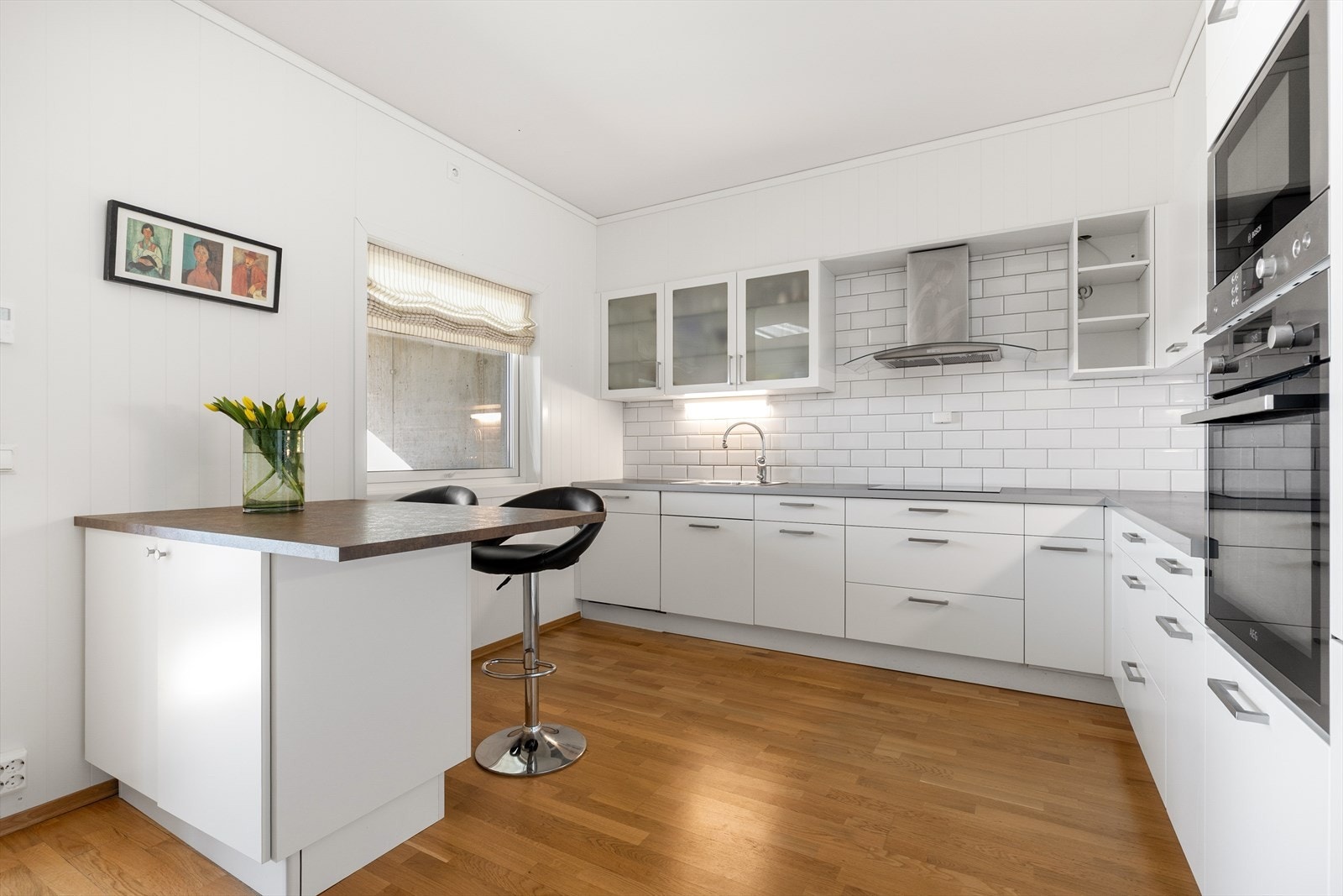 Flis på vegg over laminat benkeplate med gode arbeidsflater og nedfelt oppvaskkum. Over kokesonen er det montert komfyrvakt og ventilator. Galleribilde