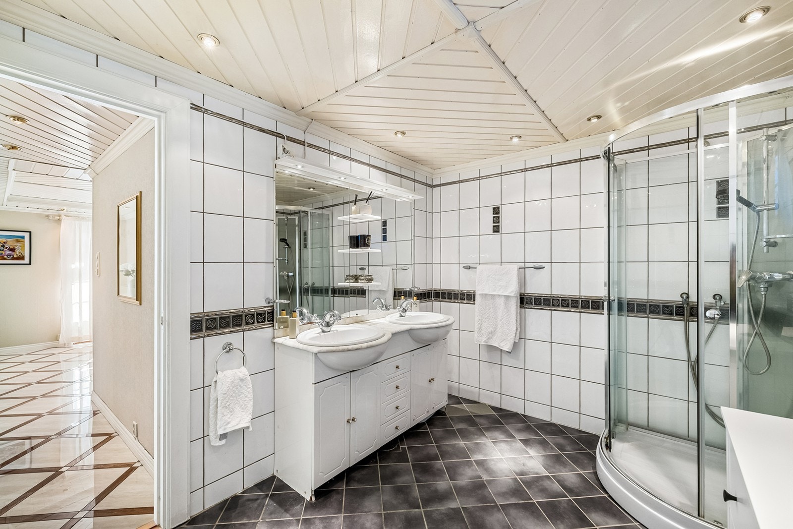 Flislagt bad med doble servanter, dusjkabinett og speil med lys. Galleribilde