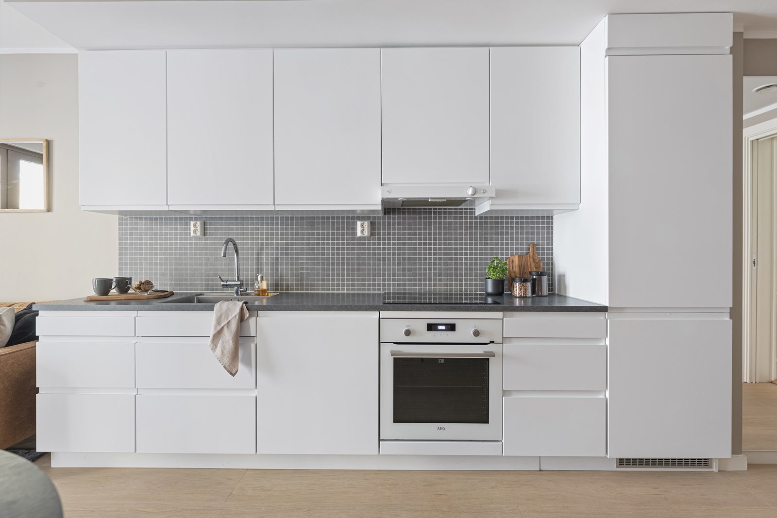 Stilrent kjøkken fra 2020 med glatte fronter, laminat benkeplate og nedfelt kum i stål. Hvitevarer som platetopp, stekeovn, oppvaskmaskin og kjøl/frys er integrert i innredningen. Galleribilde