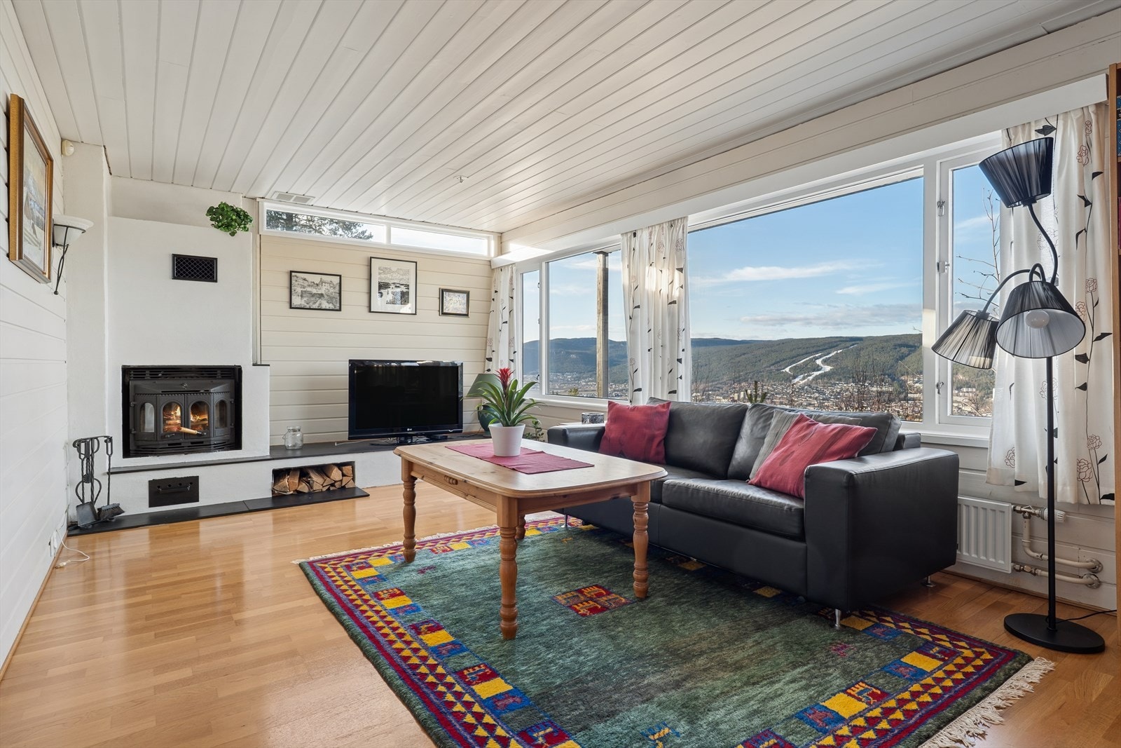 Stuen i underetasjen er et lyst og innbydende rom med store vindusflater som åpner opp mot en vidstrakt utsikt over byen. Galleribilde