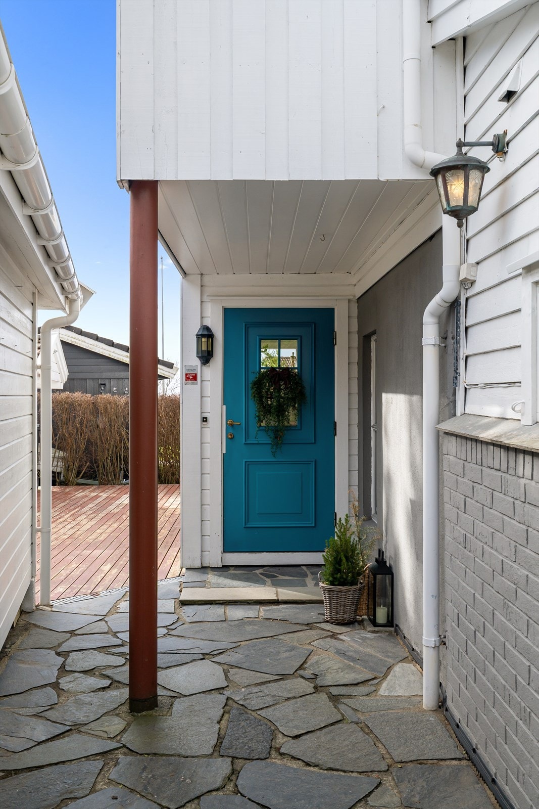 Et overbygget inngangsparti med skiferheller ønsker deg velkommen inn. Entrédøren er fra 1996. Galleribilde