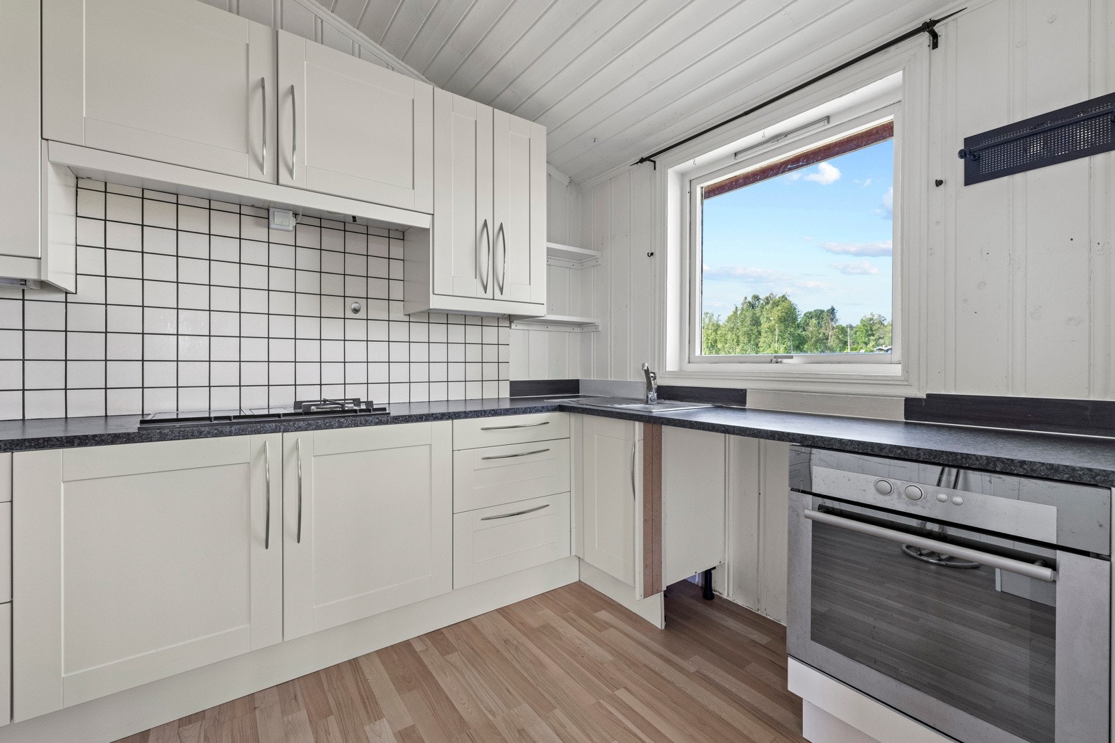 Lyst og sjarmerende kjøkken med innredning med profilerte fonter og benkeplate av laminat. Galleribilde