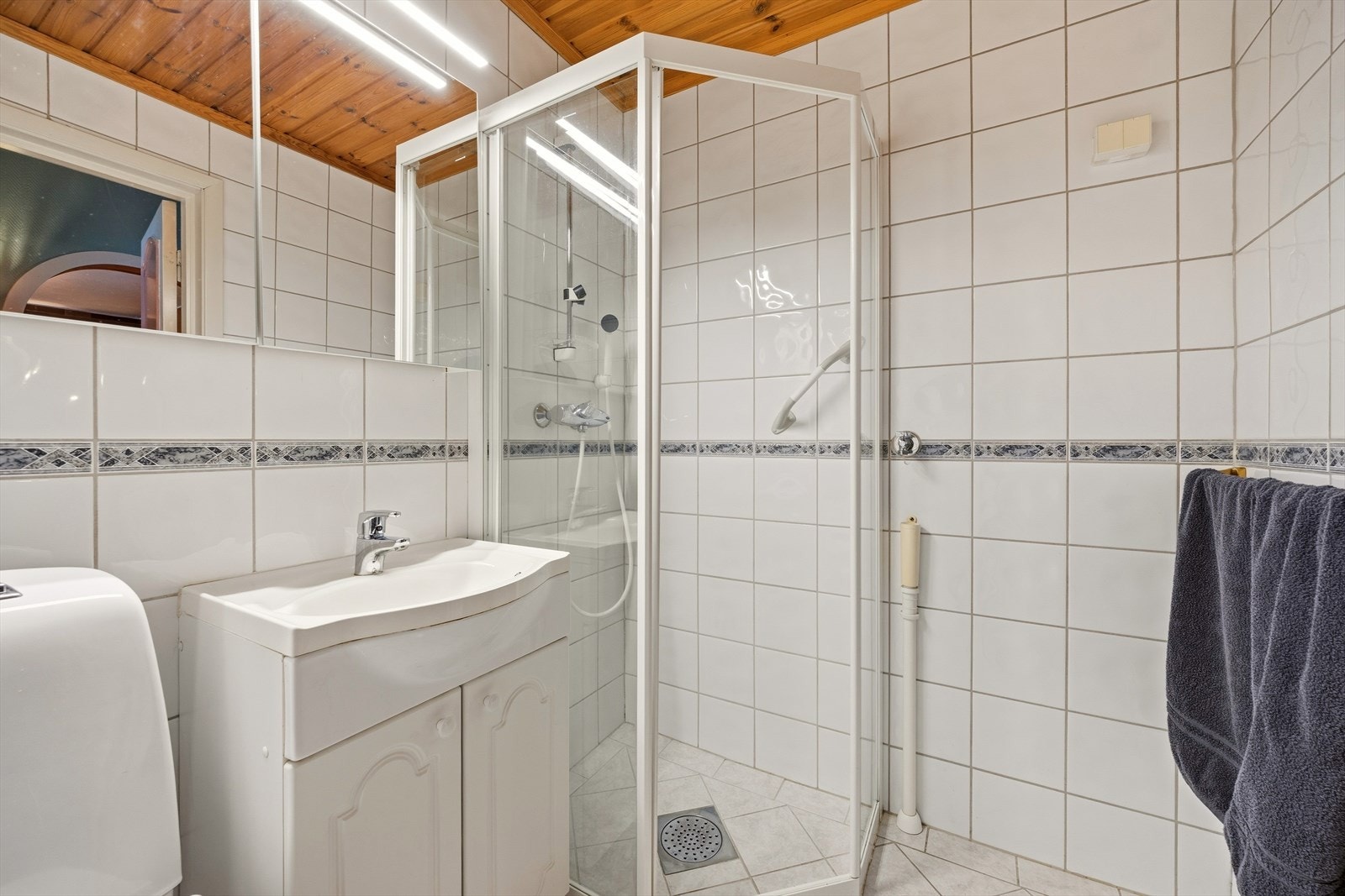 Badet er utstyrt med servant med underskap, speilskap, toalett og dusjkabinett Galleribilde