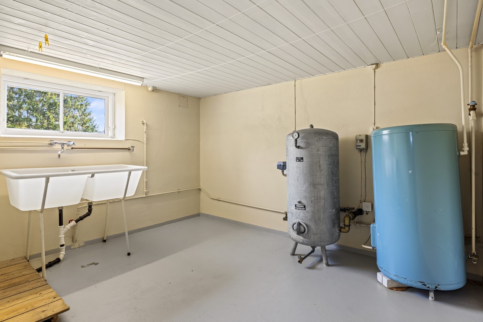 Praktisk vaskerom i kjelleren av eldre dato med malt betonggulv, utslagskum og opplegg for vaskemaskin. Varmtvannstanken på ca. 200 liter er også plassert her. Galleribilde