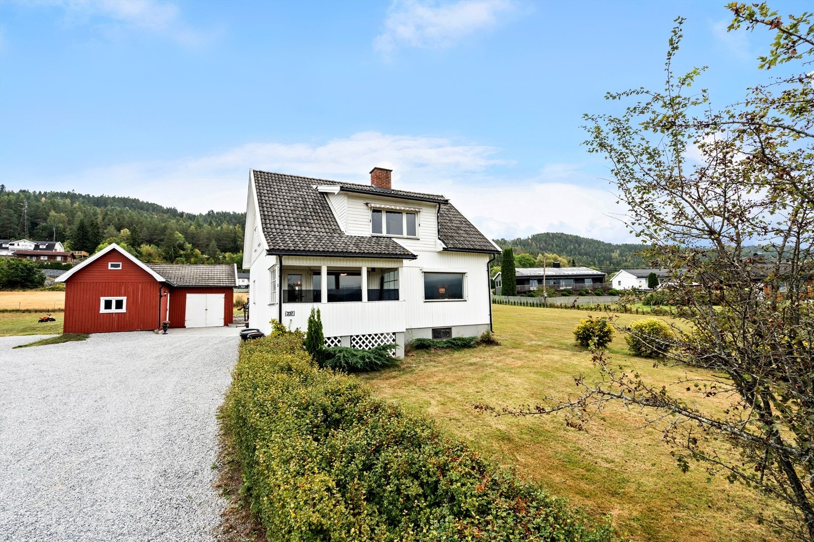 Forsiden av fasaden med gruset gårdsplass og uthus/garasje Galleribilde