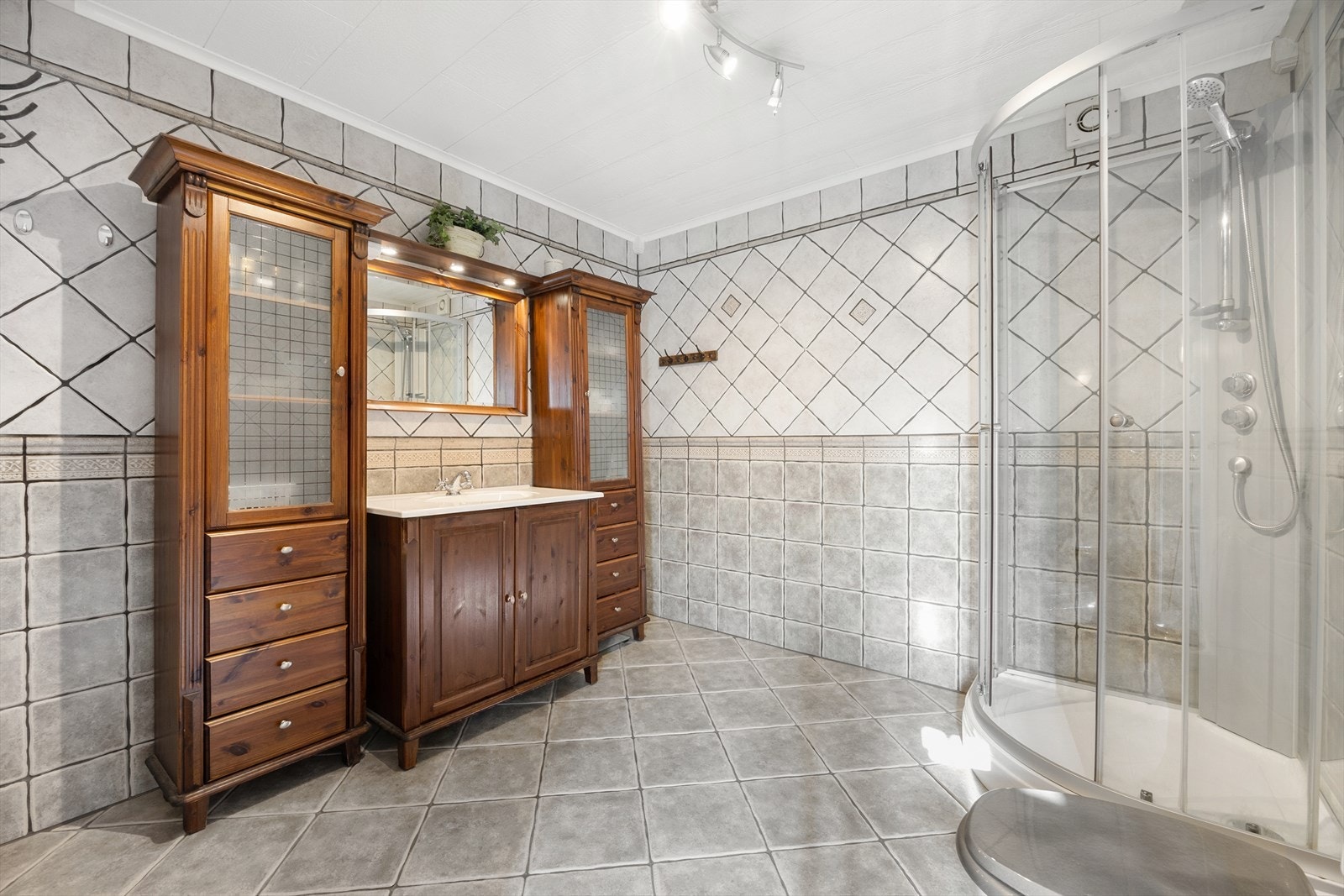 I første etasje har boligen et romslig bad og et eget praktisk vaskerom. Badet fra 2005 er innredet med vegg- og gulvfliser i ulike gråtoner. Varme er lagt i gulvet, og badet har toalett og dusjkabinett. Galleribilde