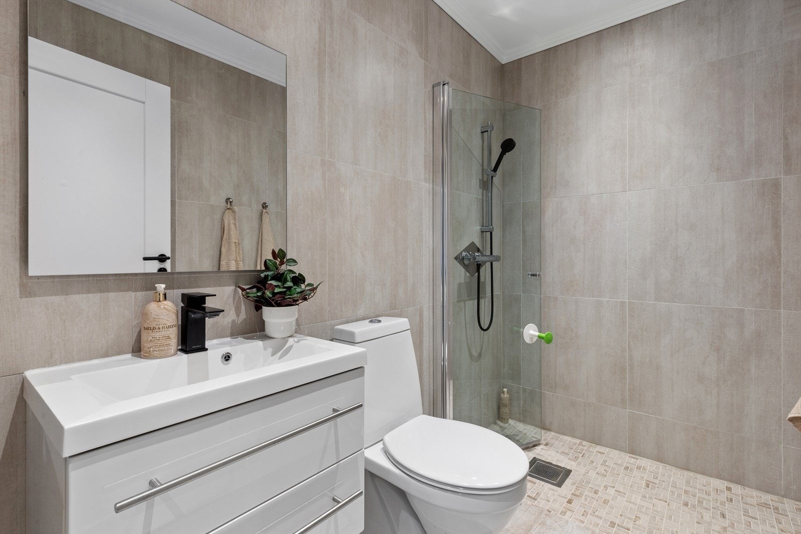 Flott baderom i underetasjen med store, moderne veggfliser i lune naturtoner som gir et stilrent og tidløst uttrykk. Dusjsonen er utført med mindre mosaikklignende gulvfliser for et harmonisk helhetsinntrykk Galleribilde