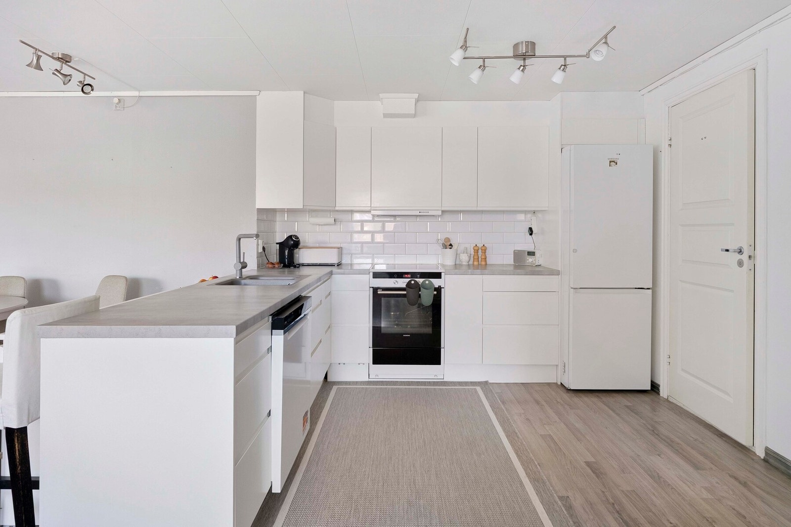 Hybelen har et kompakt kjøkken med hvite, slette fronter og laminat benkeplate, samt frittstående hvitevarer. Galleribilde