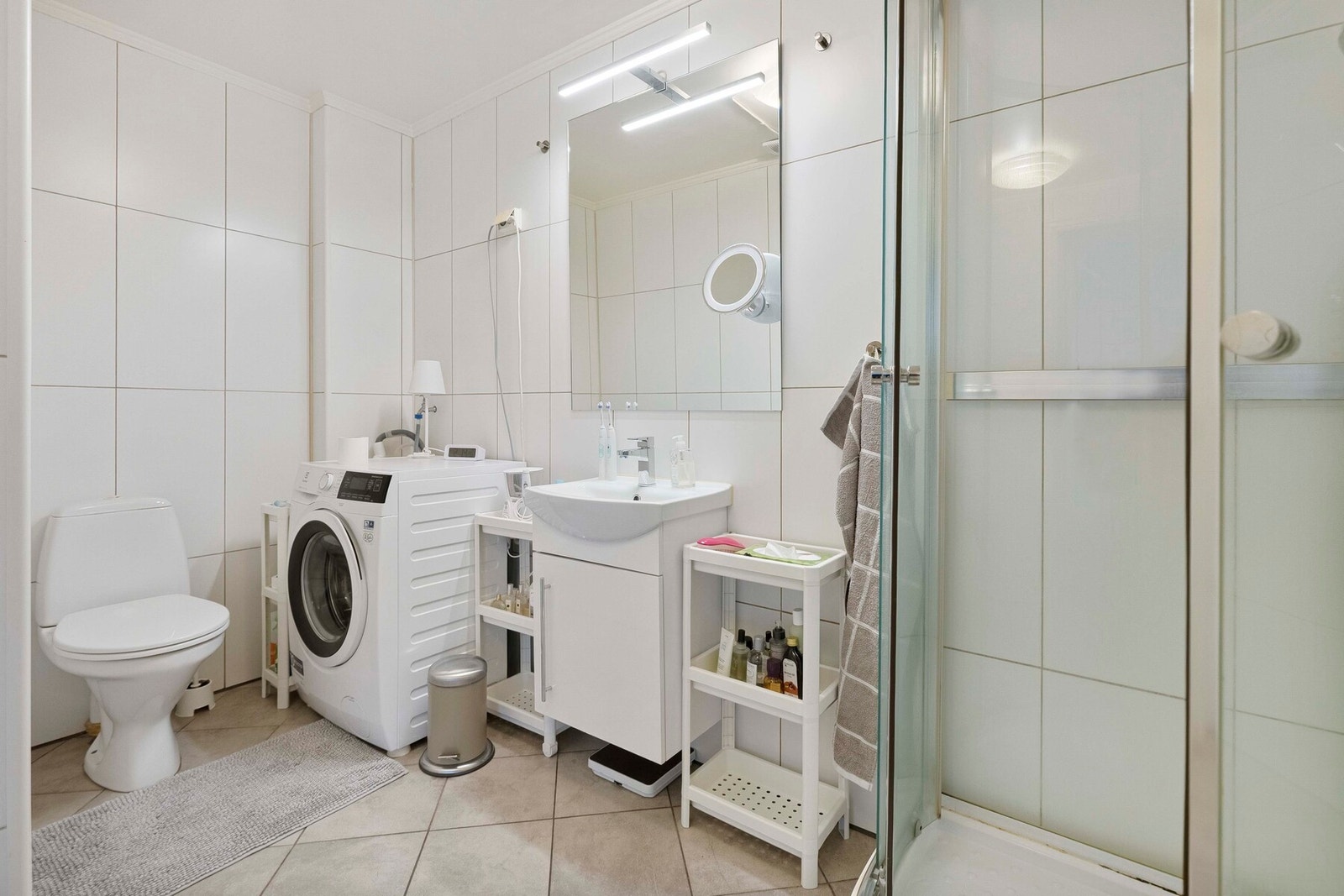 Bad/vaskerommet er praktisk innredet med flislagte overflater, dusjkabinett, toalett, baderomsmøbel og opplegg for vaskemaskin. Galleribilde
