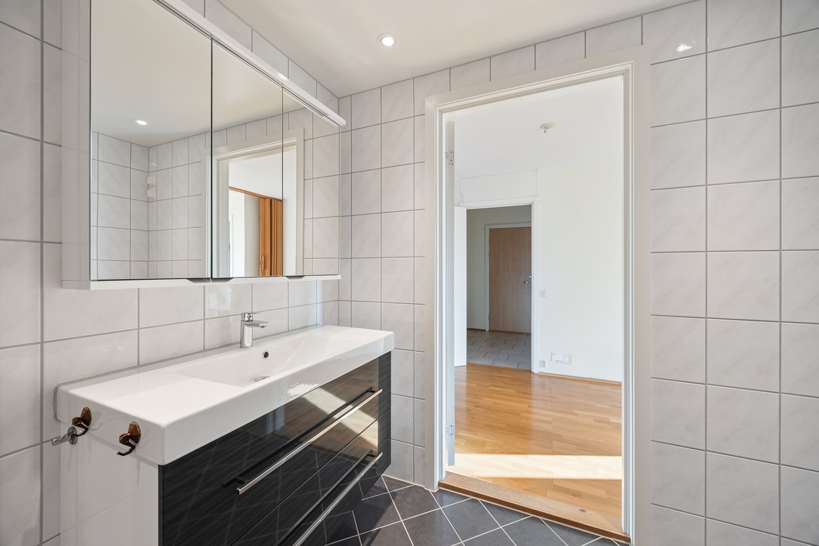 Badet er innredet med servantskap med ett-greps blandebatteri, speilskap, avskjermet dusjhjørne med glass, blandebatteri og dusjgarnityr. Galleribilde