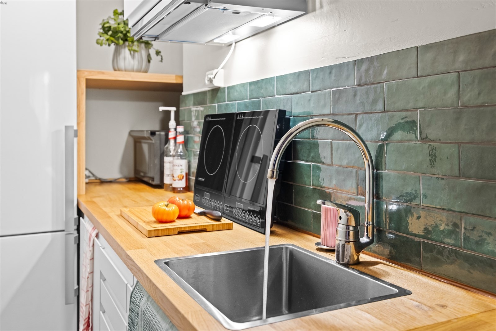 Kjøkkenet er utstyrt med nedfelt kum i rustfritt stål, fliser på vegg over benkeplaten og belysning via ventilator. Galleribilde