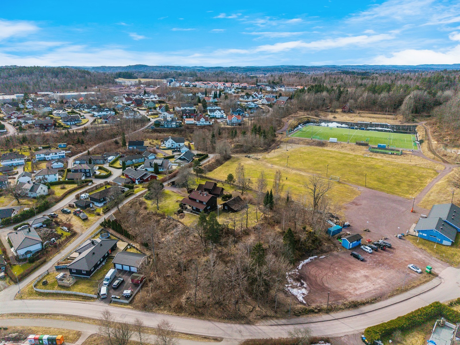 Tomten grenser inn mot idrettsanlegget og skogen med turstier og lysløype Galleribilde
