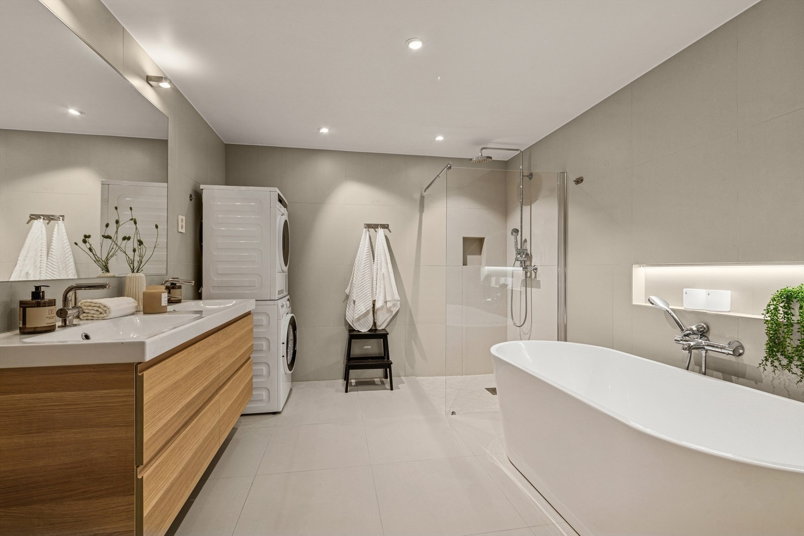 Stort baderom med dushjørnet med regnfall- og hånddusj, badekar med hånddusj og tappekran, dobbelservant med underskuffer, vegghengt speil, vegghengt wc med innbygget sisterne, samt opplegg for vaskemaskin og tørketrommel. Galleribilde