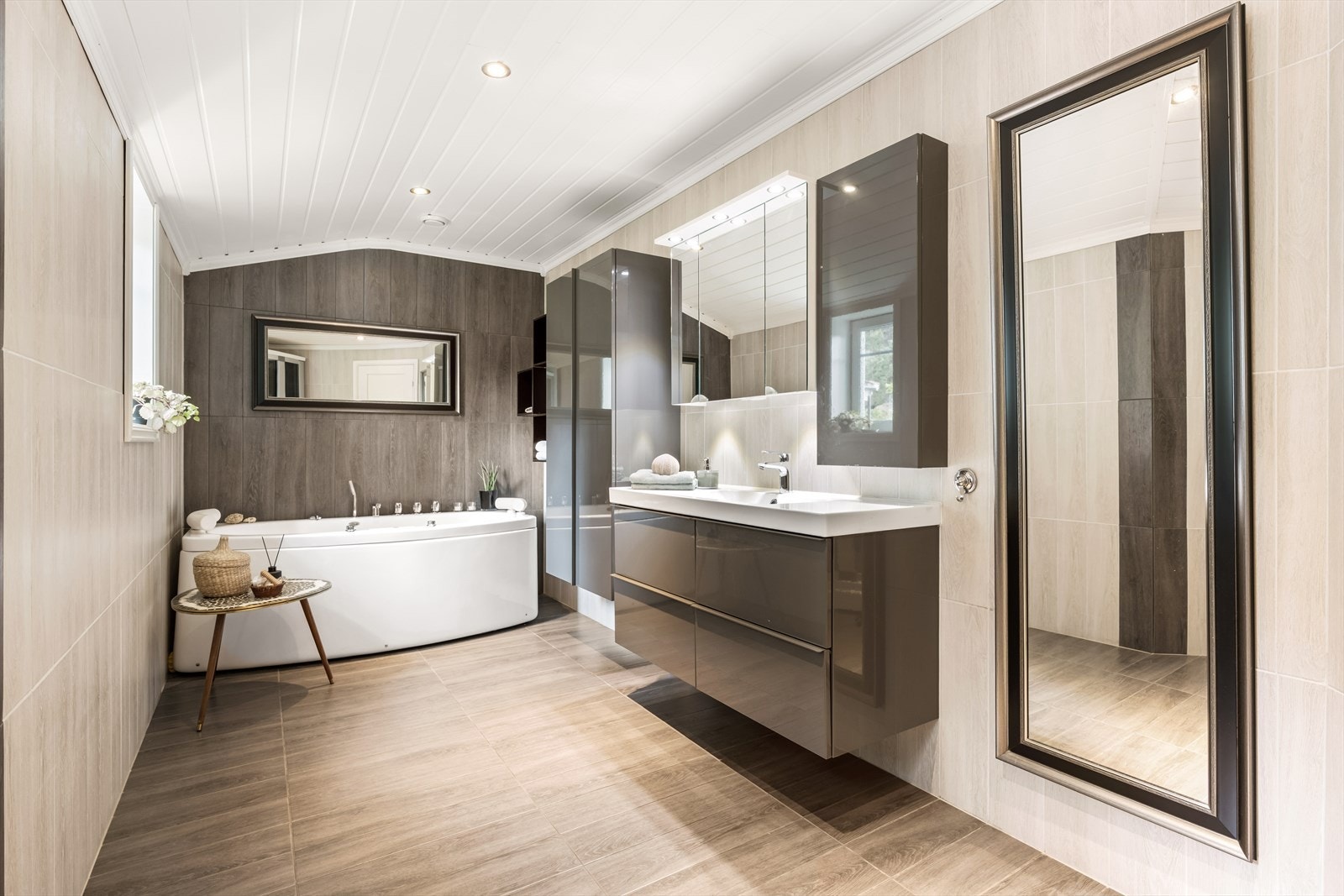 Badet er innredet med baderomsinnredning med heldekkende nedfelt servant med oppbevaring, speilskap, vegg hengt toalett, boblekar og steamdusj Galleribilde