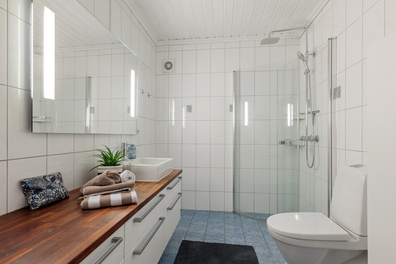 Badet i underetasjen er flislagt og har dusjhjørne, toalett og baderomsinnredning. Et praktisk og pent bad med et godt og moderne uttrykk Galleribilde