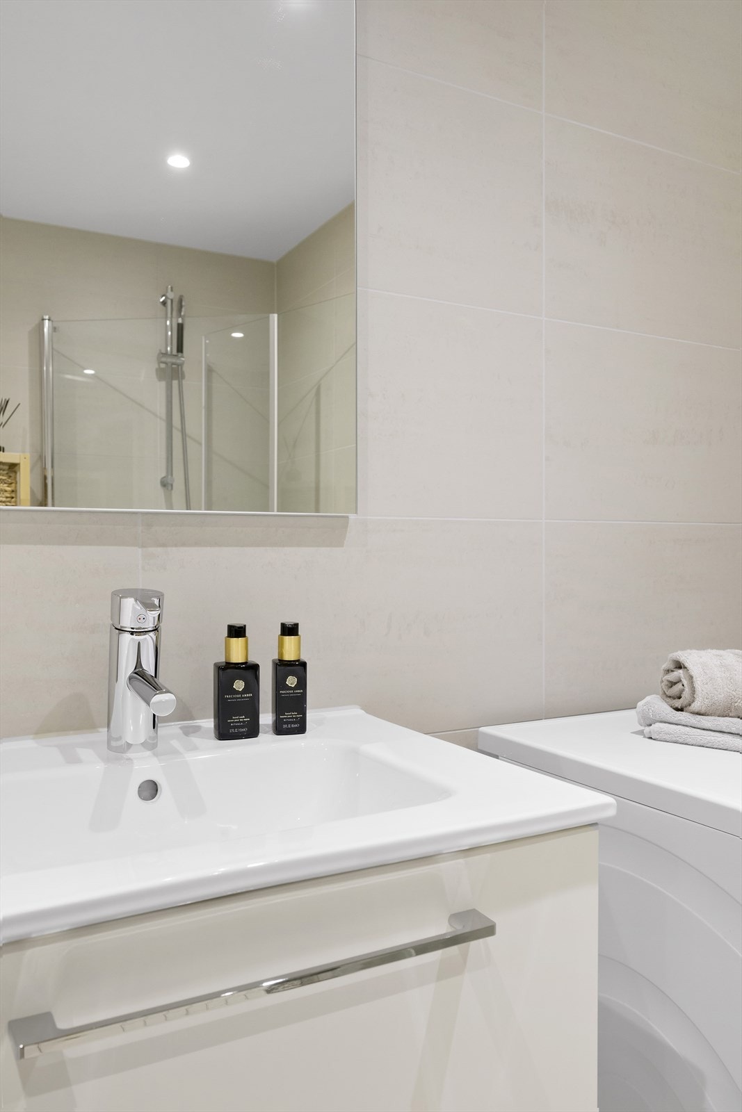 Slett lys innredning med servant og speil med lys over, veggmontert toalett og dusjnisje. Det er i tillegg opplegg for vaskemaskin. Galleribilde