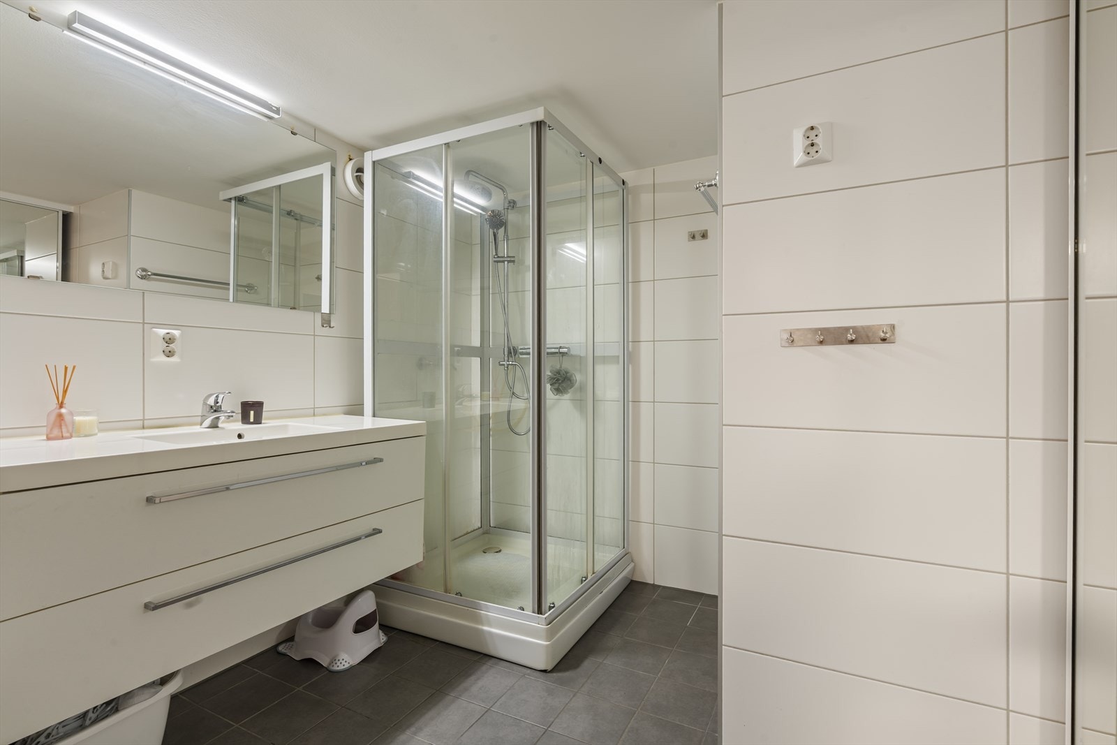 Bad/vaskerom er lyst og pent med fliser på gulv og vegger og elektriske varmekabler Galleribilde