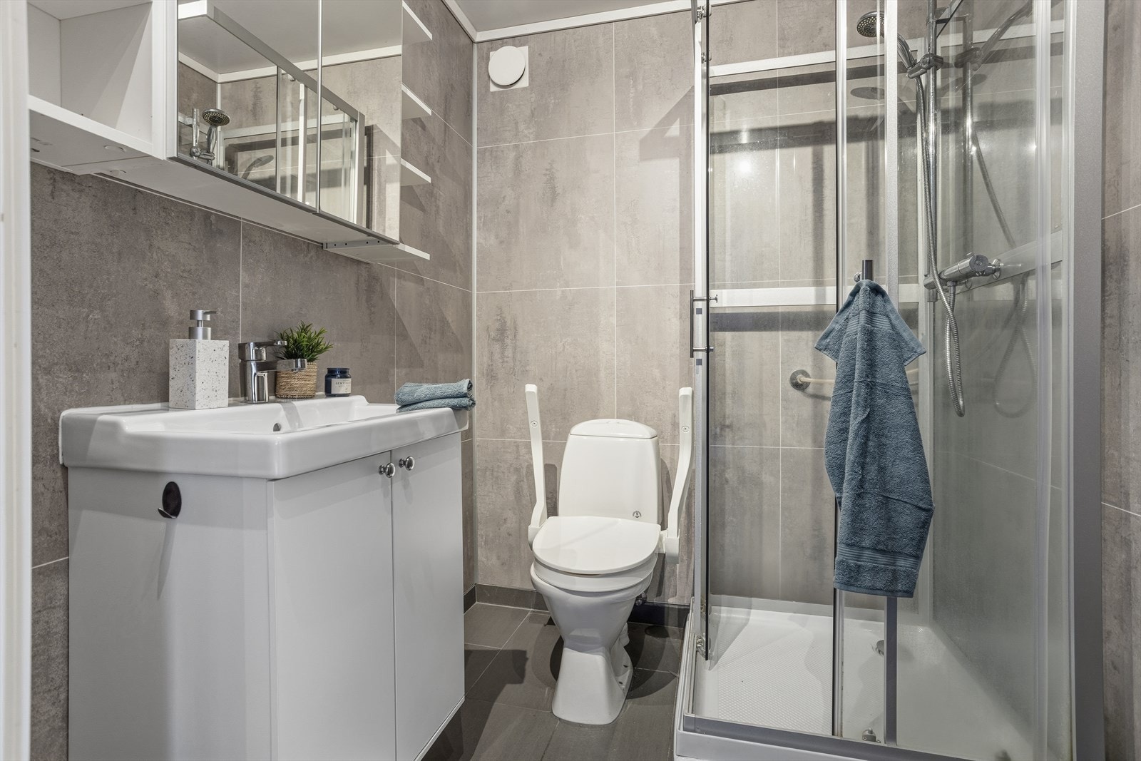 Det moderne baderommet har delikate grå fliser og et praktisk dusjkabinett som gir en ren og tidløs atmosfære. Galleribilde