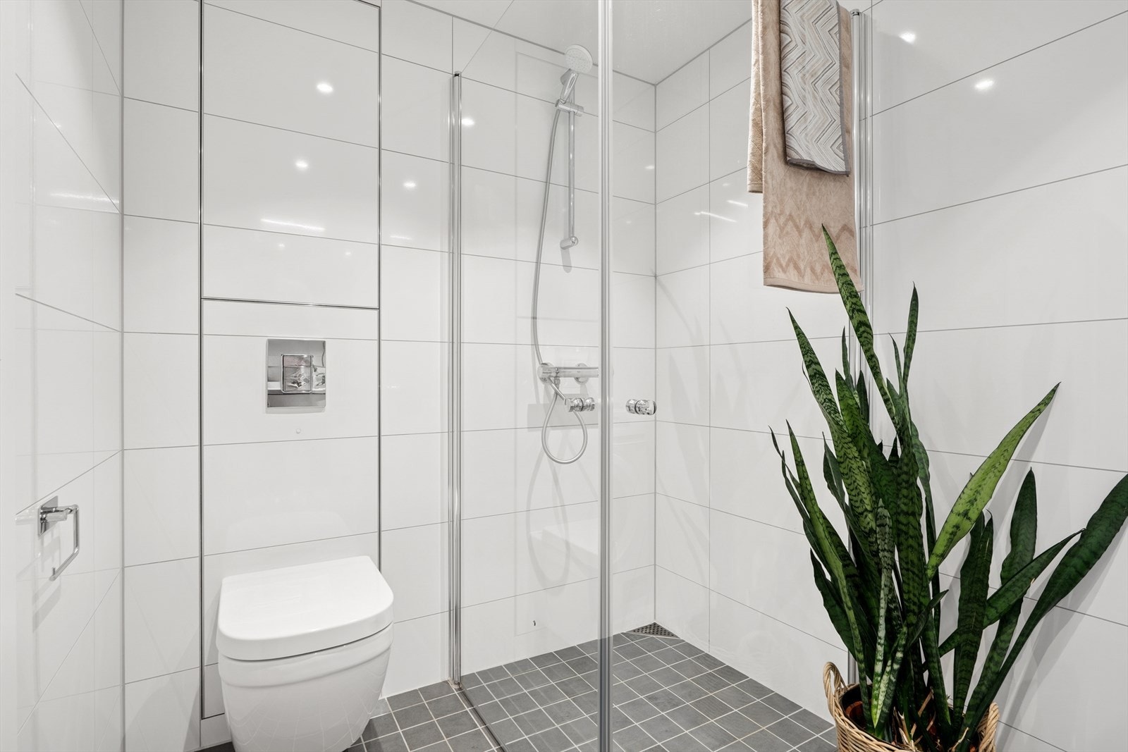 Badet er helfliset med hvite fliser på veggene og grå fliser på gulvet, og har behagelig gulvvarme. Downlights i himlingen gir god og stemningsfull belysning. Galleribilde