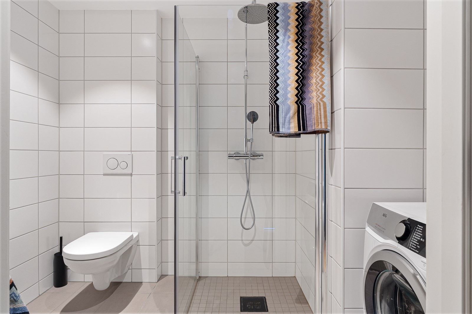 Badet er innredet med vegghengt toalett, dusj med flass foldedører, servant med møblement, speil med belysning, og opplegg for vaskemaskin. Galleribilde