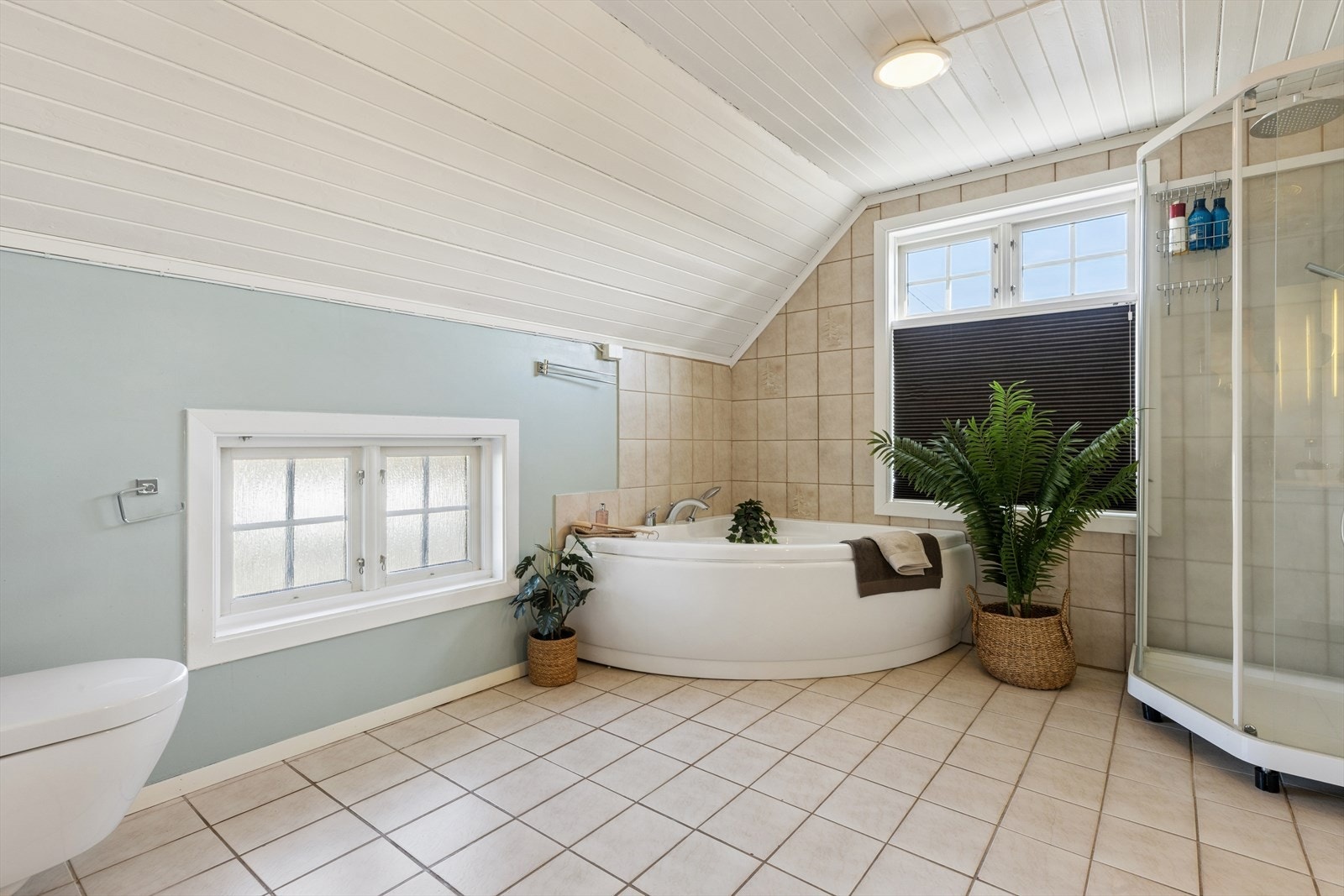 Dette badet er innredet med dusjkabinett, hjørnemontert badekar, vegghengt toalett og servant nedfelt i baderomsinnredning med speil. Galleribilde