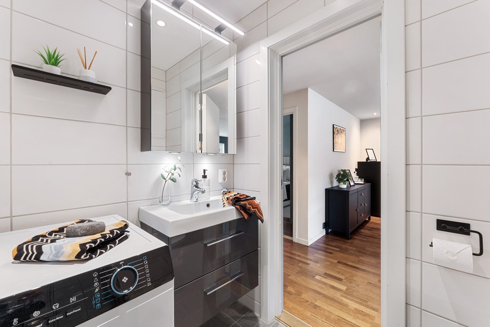 Badet er innredet med vegghengt toalett, servant med baderomsinnredning, belyst speil, dusjhjørne, opplegg for vaskemaskin og varmekabler i gulvet. Galleribilde