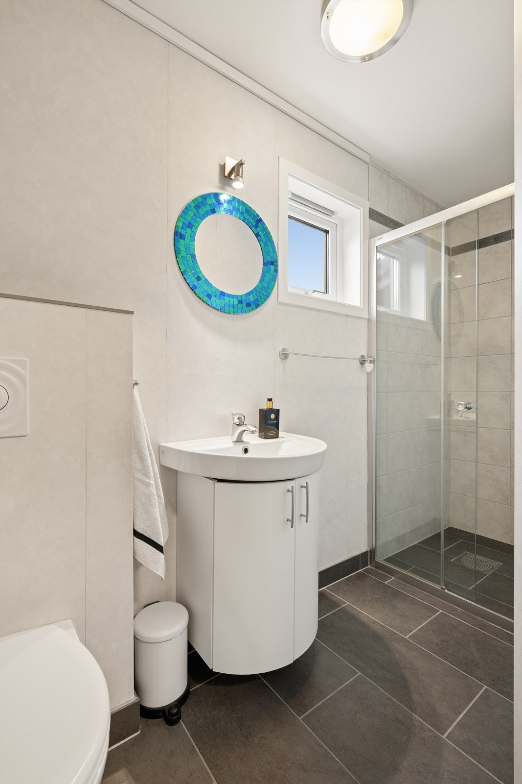 Det ene av boligens i alt tre baderom, utstyrt med dusjhjørne, vegghengt toalett og baderomsinnredning med servant. Galleribilde