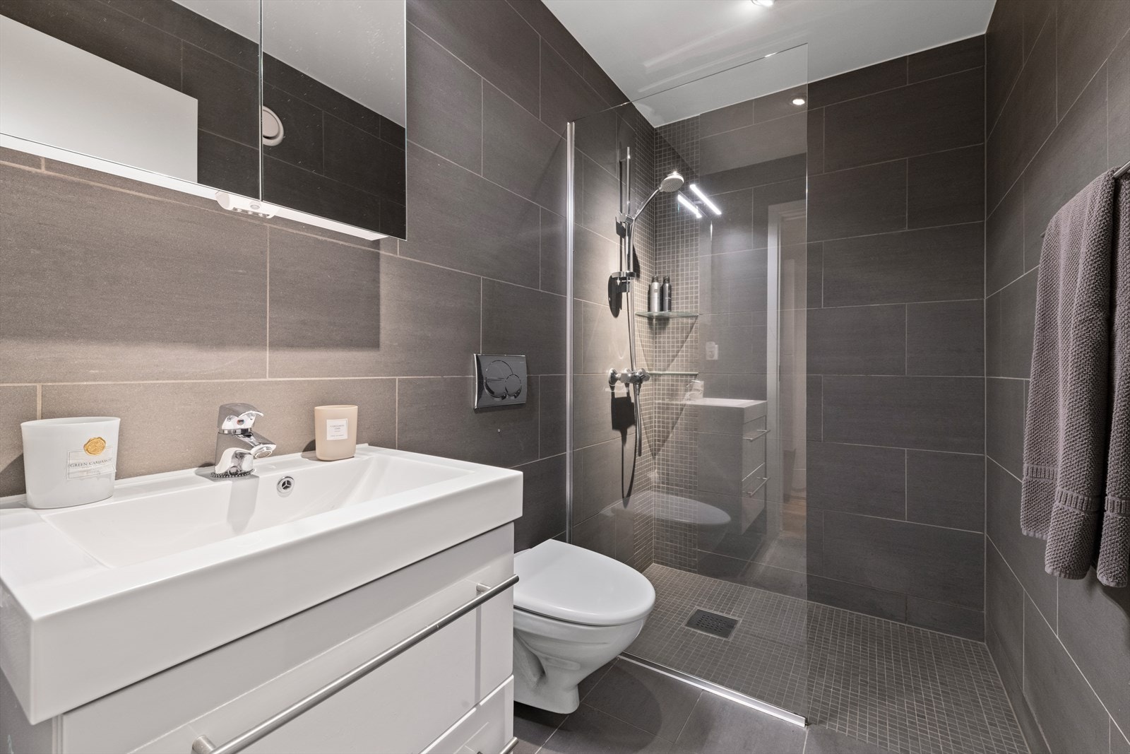 Badet i 1. etasje har innredning med helstøpt servant på skuffeinnredning, speilskap, lys, dusjhjørne med glassvegg og vegghengt toalett. Galleribilde