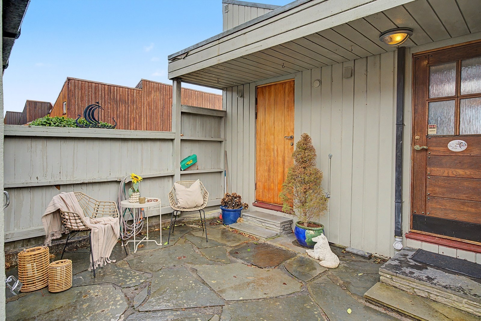 Ved inngangspartiet får du en herlig lun uteplass. Herfra kan du gå inn hoveddøren til høyre eller direkte til vaskerom og kjøkken gjennom døren til venstre. Galleribilde