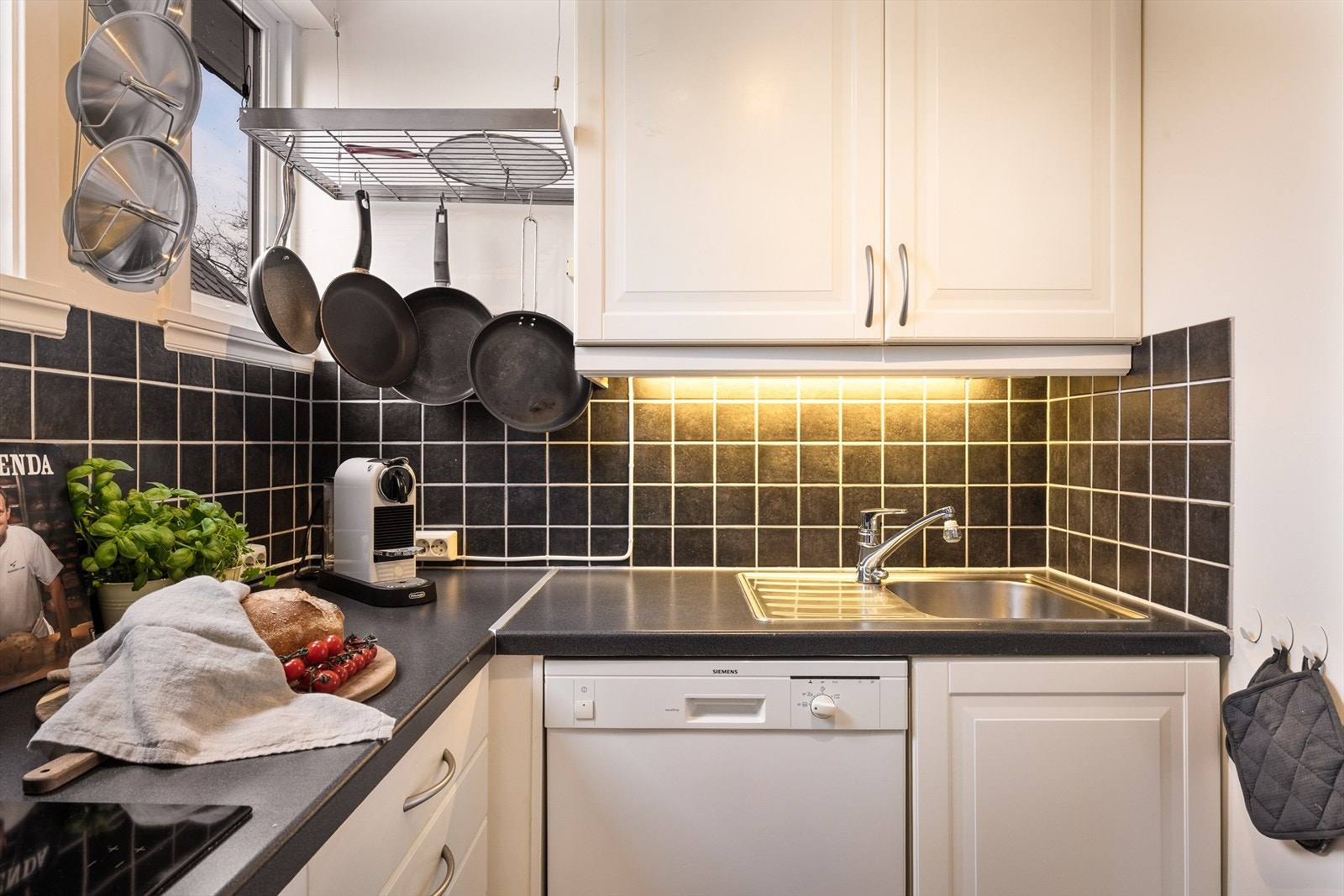 Ikea kjøkken i hvit profilert utførelse med takhøye skap og mørk laminat benkeplate med fliser over. Galleribilde