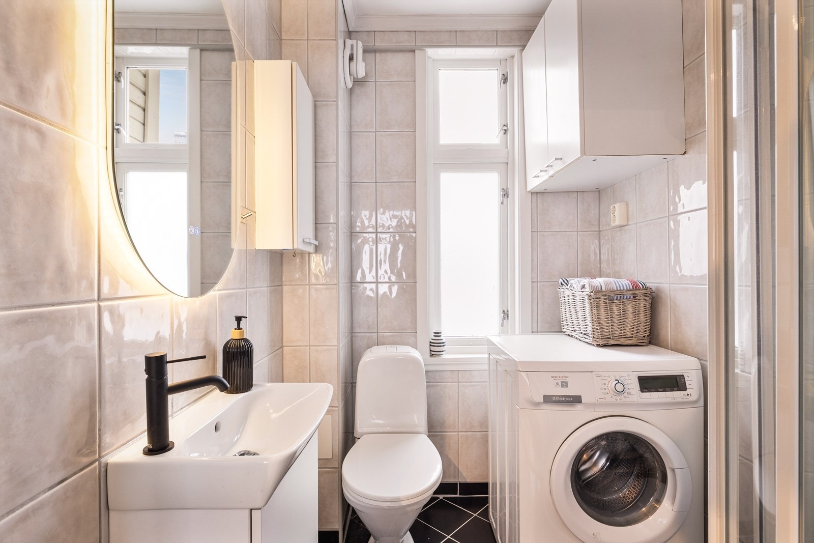 Helfliset bad innredet med baderomsinnredning med servant, toalett, dusj og opplegg for vaskemaskin. Galleribilde