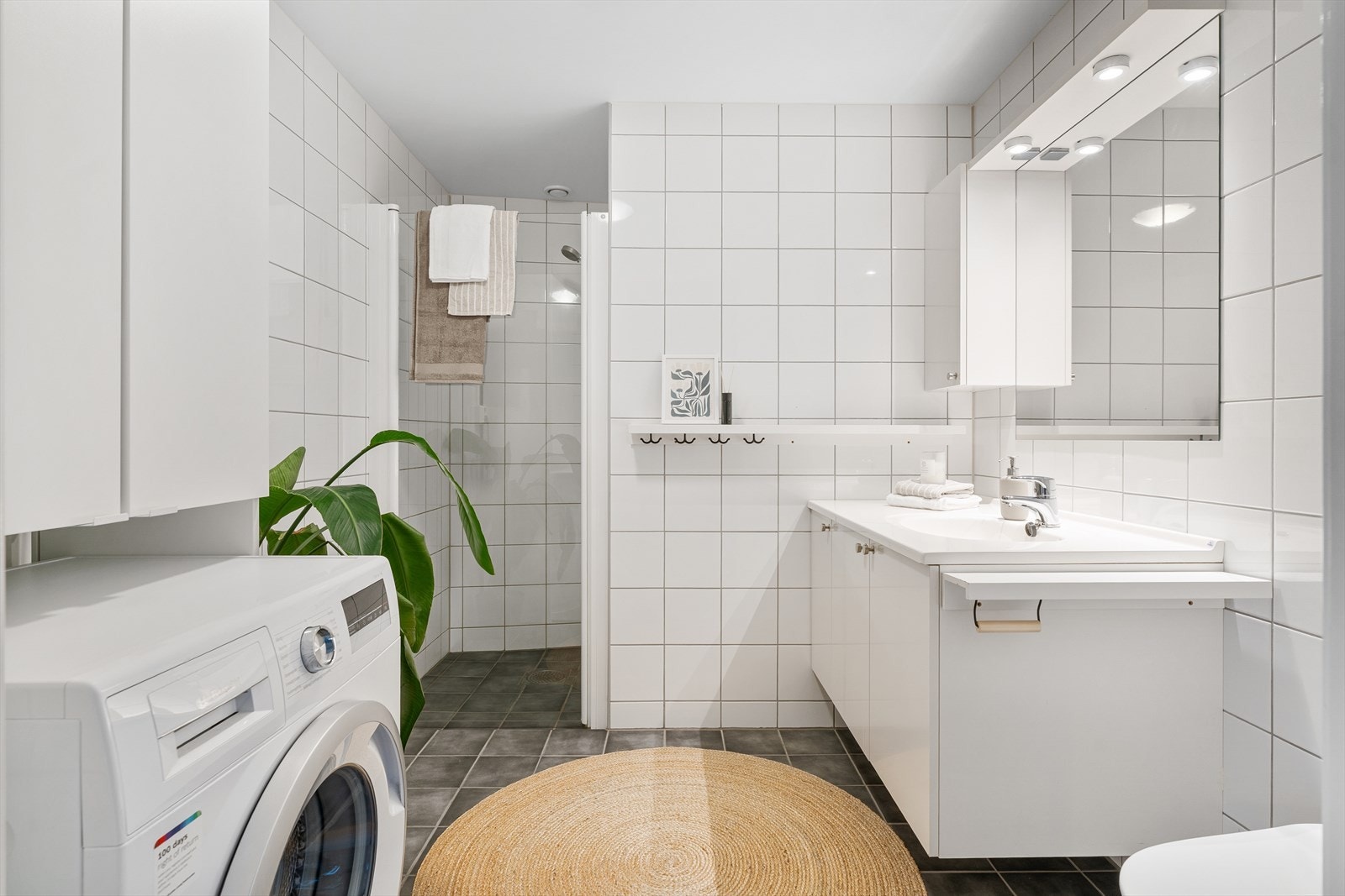 Flislagt bad med behagelig gulvvarme. Videre er det vegghengt klosett, dusjnisje, innredning med servant og opplegg for vaskemaskin/tørketrommel. Galleribilde