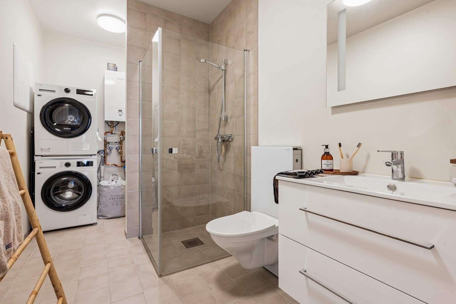 Kombinert bad og vaskerom med flislagt gulv, dusjhjørne og opplegg for vaskemaskin. Galleribilde