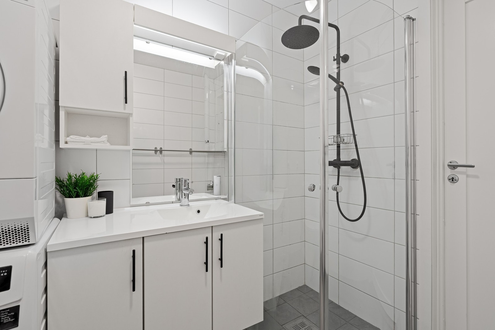 Badet er innredet med dusjhjørne, servant med tilhørende møblement, toalett og opplegg for vaskemaskin og tørketrommel. Galleribilde