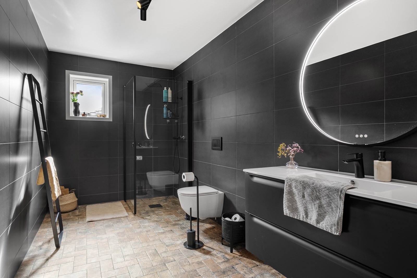 Stort og elegant bad med sorte fliser, rund LED-speil og moderne innredning i stramt, nordisk uttrykk. Galleribilde