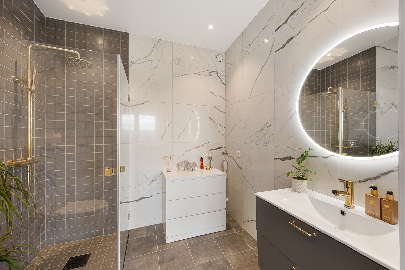 Det andre badet har hvite marmorfliser på veggene, downlights, grå fliser i dusjsonen og matchende fliser på gulv med gulvvarme. Galleribilde