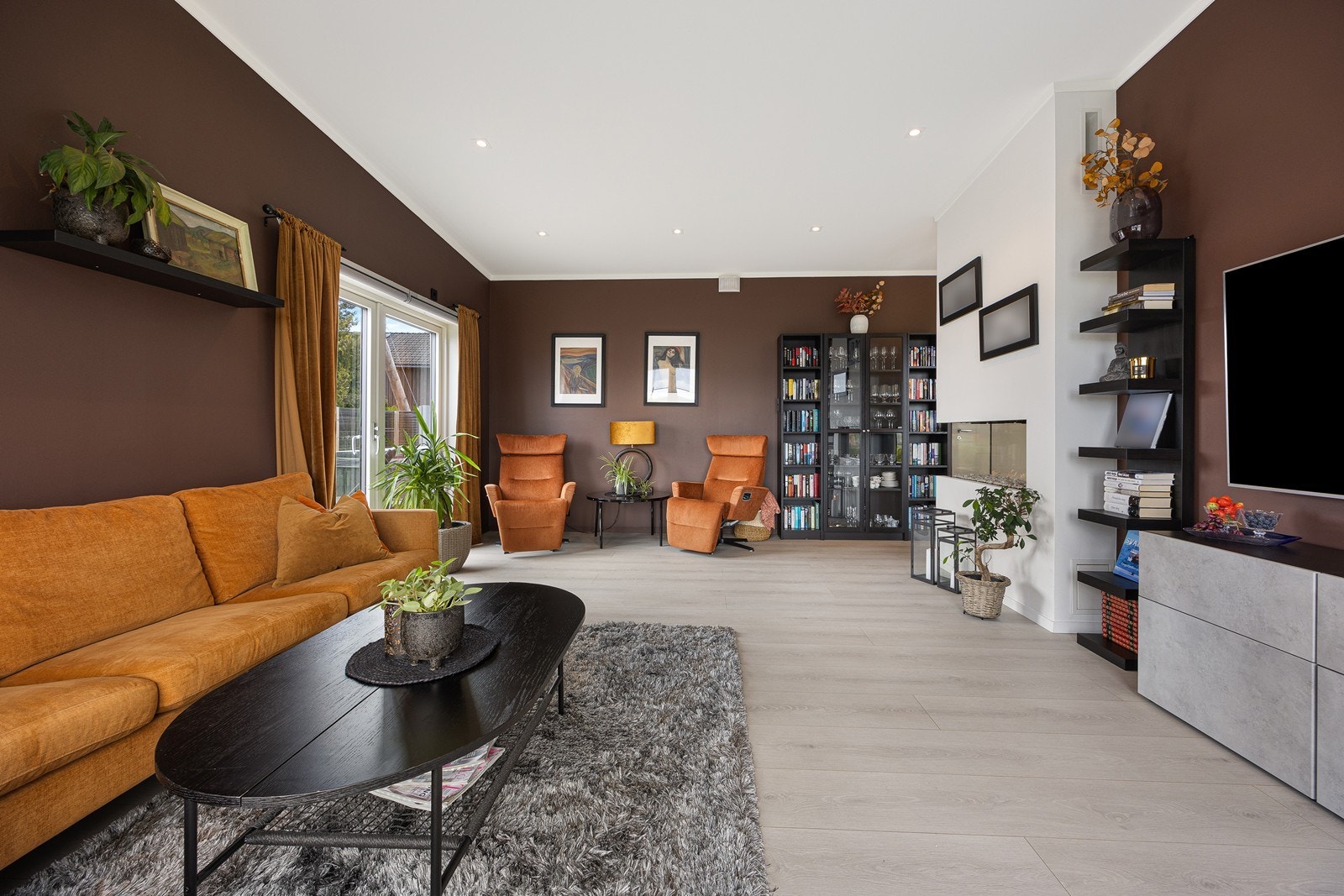 Veggene i allrommet er malt i varme jordtoner, og det er lys, enstavs laminat på gulv med gulvvarme - en komfortdetalj som er gjennomgående for hele boligen. Galleribilde