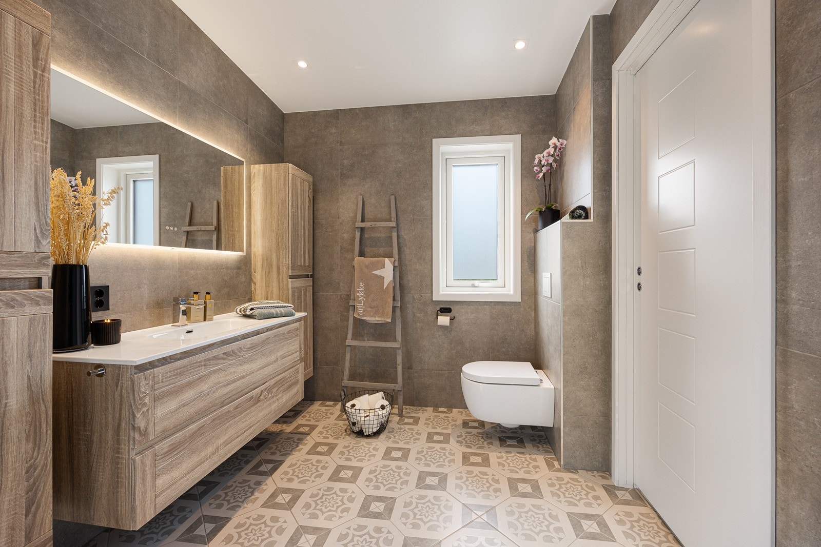 Dette badet er tilknyttet hovedsoverommet. Her er det sandfargede fliser på veggene, downlights i himlingen og mønstrede fliser på gulv med gulvvarme. Galleribilde