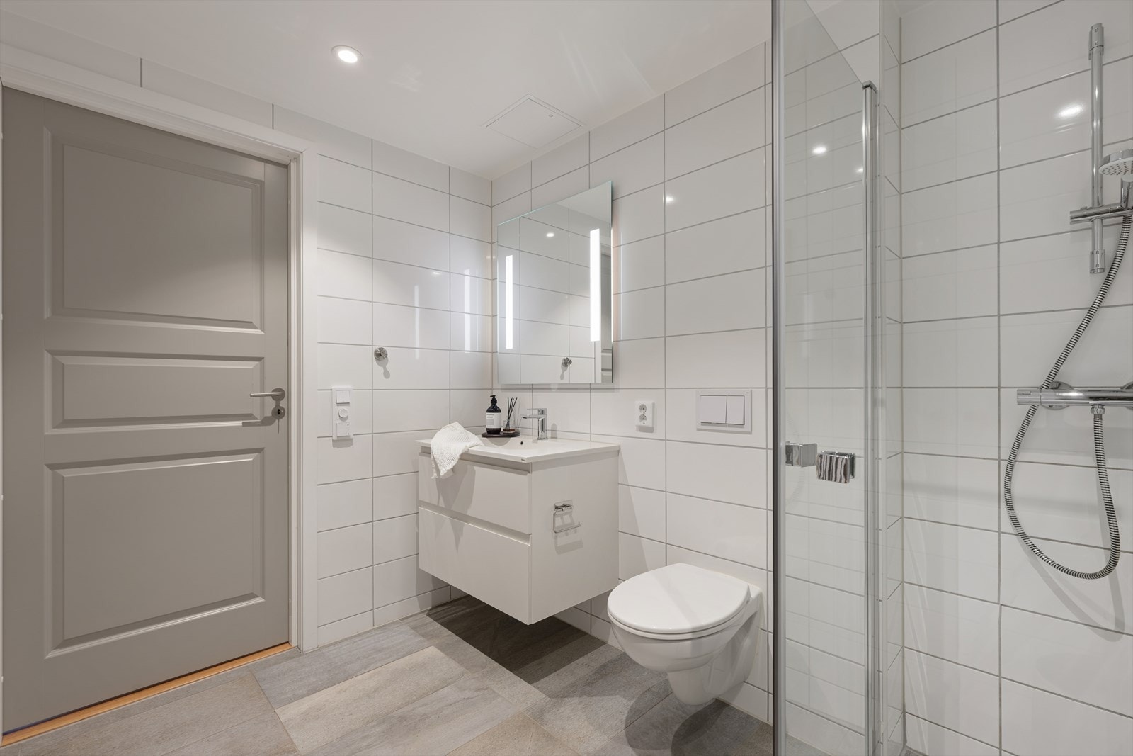 Badet er fra byggeåret med flislagte overflater, vegghengt toalett og dusjhjørne med innfellbare vegger. Galleribilde