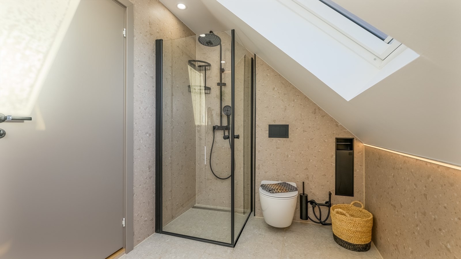 Badet er ellers utstyrt med dusjhjørne, vegghengt toalett og baderomsinnredning med nedfelt servant. I tillegg har man opplegg for vaskemaskin. Her er sorte detaljer gjennomgående, som sammen med stilig ledbelysning gir et stramt og moderne uttrykk. Galleribilde