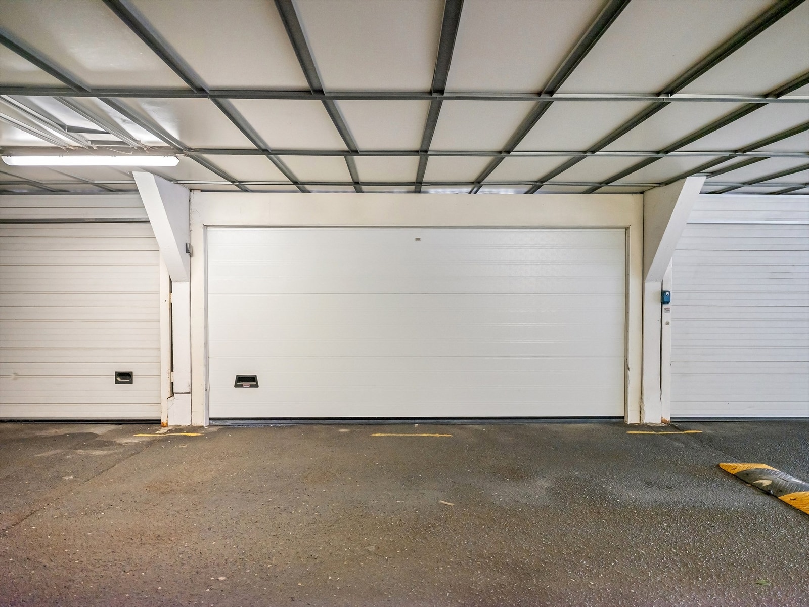 Garasjeplassen er lukket med automatisk leddport, og er plassert like ved døren til blokken. Porten er dobbel og deles med naboen Galleribilde