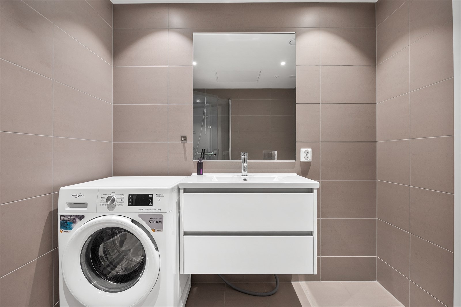 Badet er helfliset og har opplegg for vaskemaskin ved siden av en moderne servantinnredning. Galleribilde