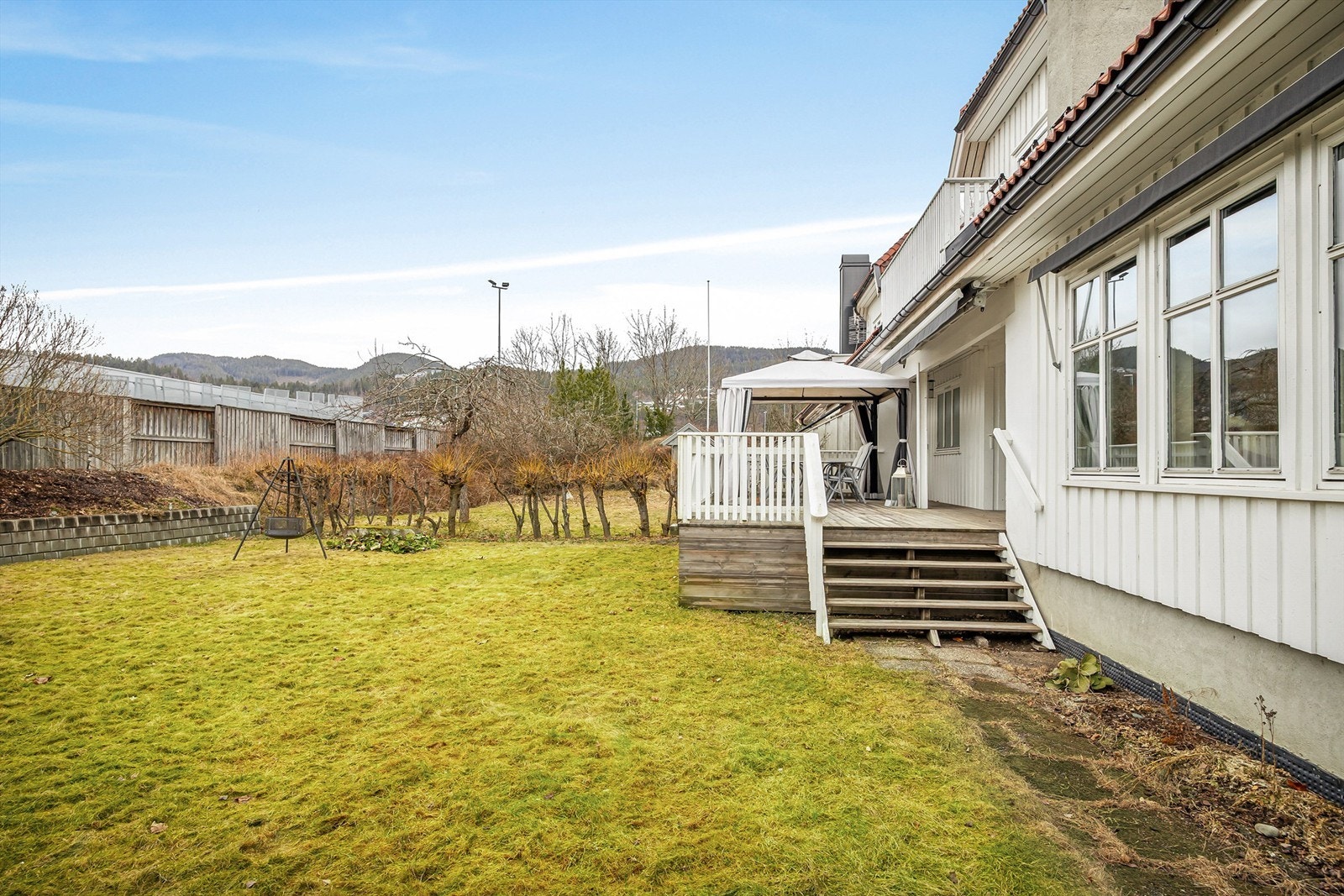 Tilnærmet flat tomt opparbeidet med gruset gårdsplass, plenarealer og diverse beplantning Galleribilde