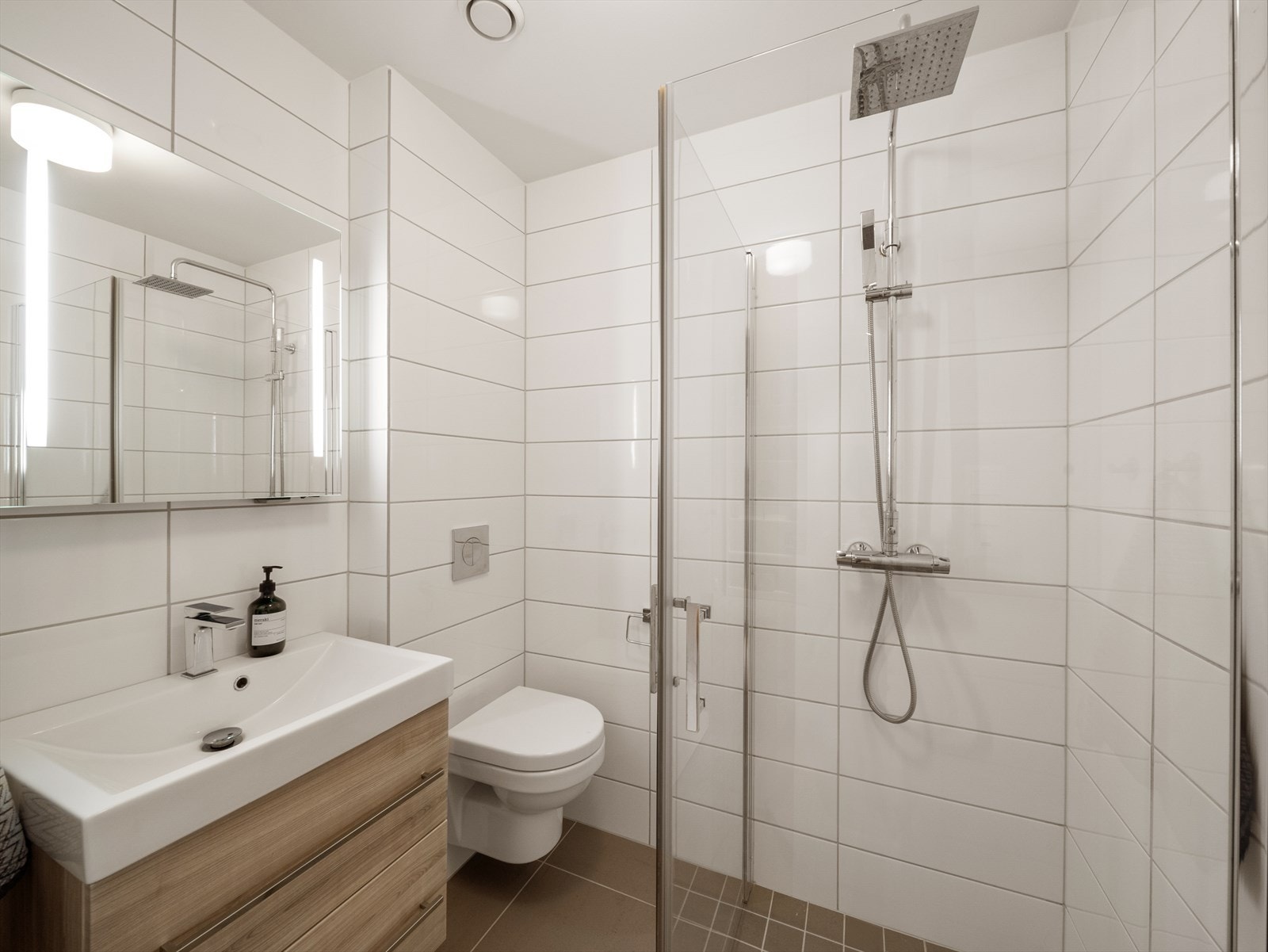 Helfliset baderom i u. etasje med vegghengt toalett, pen innredning og dusjhjørne med glassvegg. Galleribilde