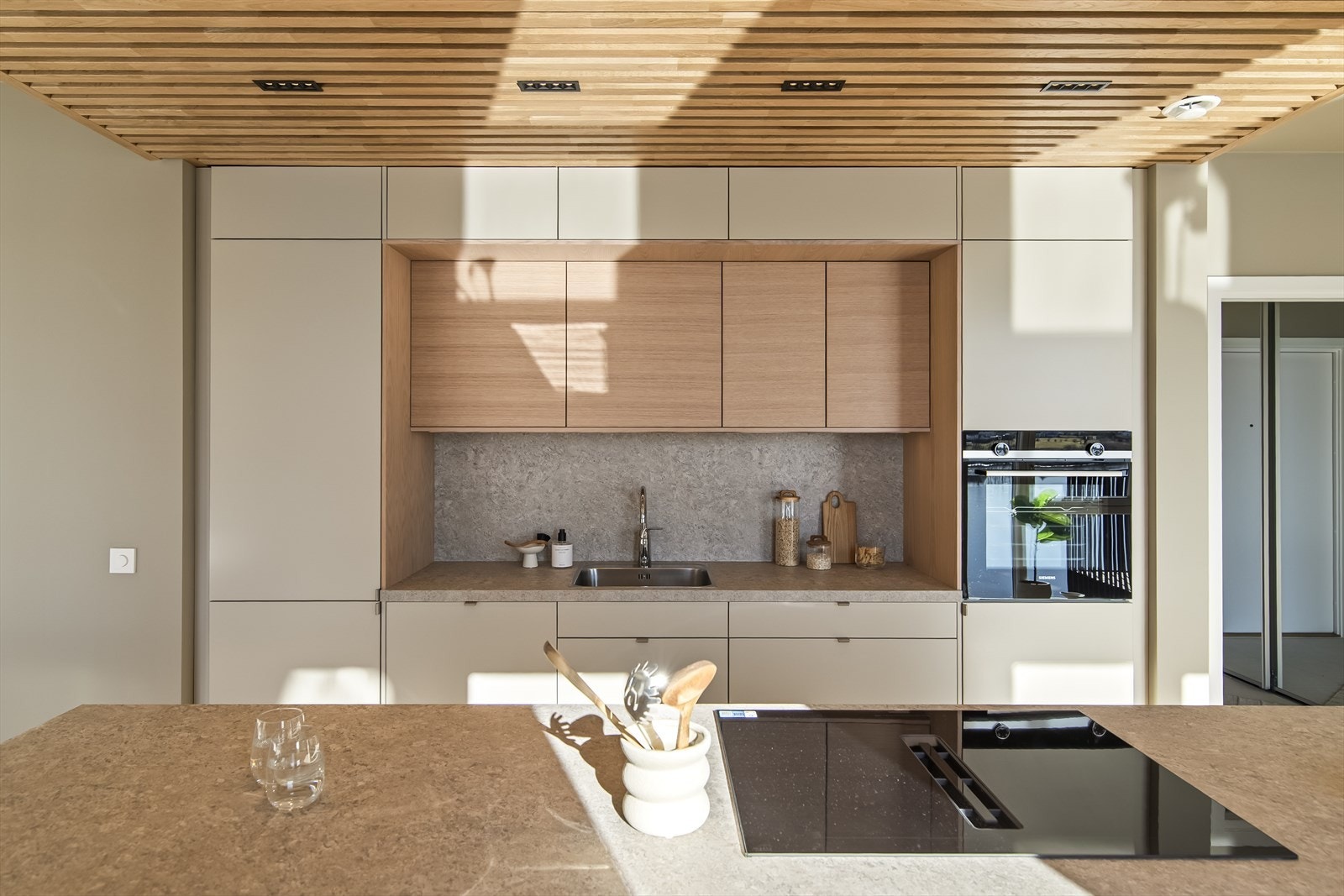 Innredningen er av typen Bistro levert av Drømmekjøkken, med oppvaskkum av rustfritt stål, mønstret benk i grått design og glatte, beige fronter som matcher veggene. Galleribilde