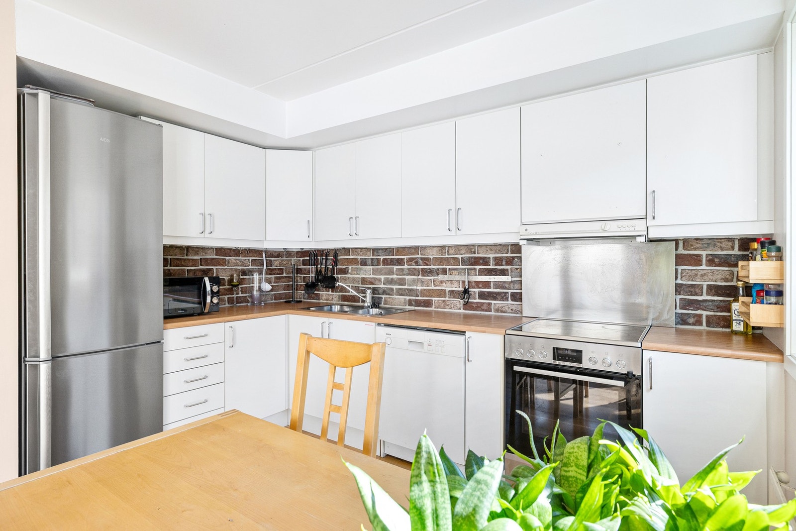 Kjøkkeninnredning med laminerte skrog og slette fronter. Laminat benkeplate med nedfelt oppvaskkum og glassplate på veggen over vaskesonen. Galleribilde