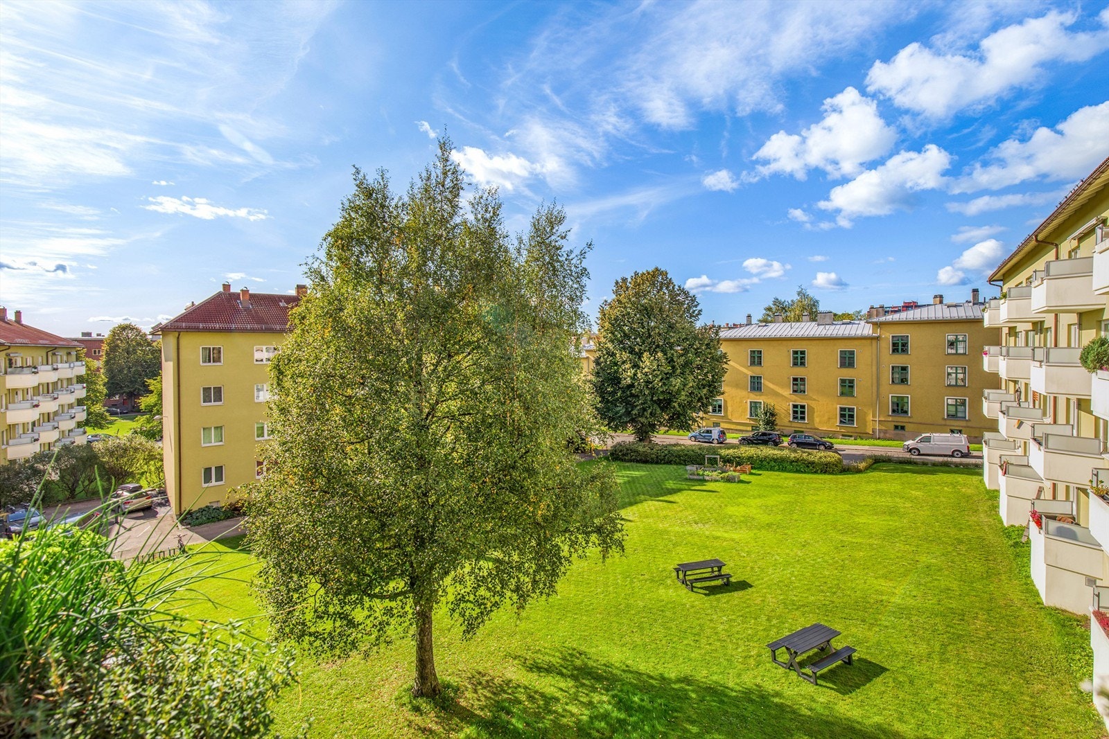 Fra balkongen ser du ut over borettslagets fellesareal. Fellesarealene mellom blokkene er pent opparbeidet med gressplener, sittegrupper og ulik beplantning. Galleribilde