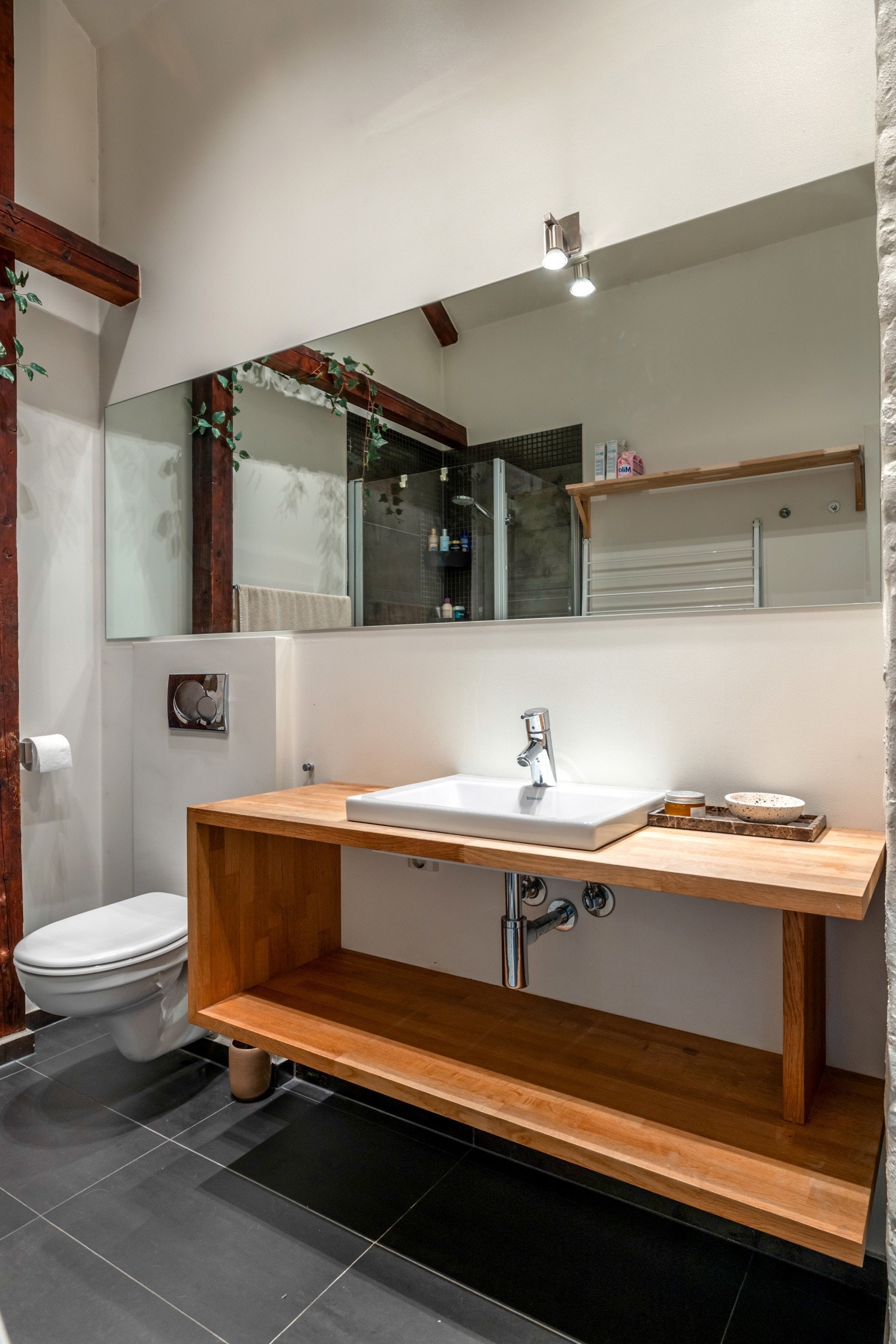 En stilren servant med benkeplate i tre gir varme til uttrykket, mens åpne hyller bidrar til gode oppbevaringsmuligheter. Galleribilde