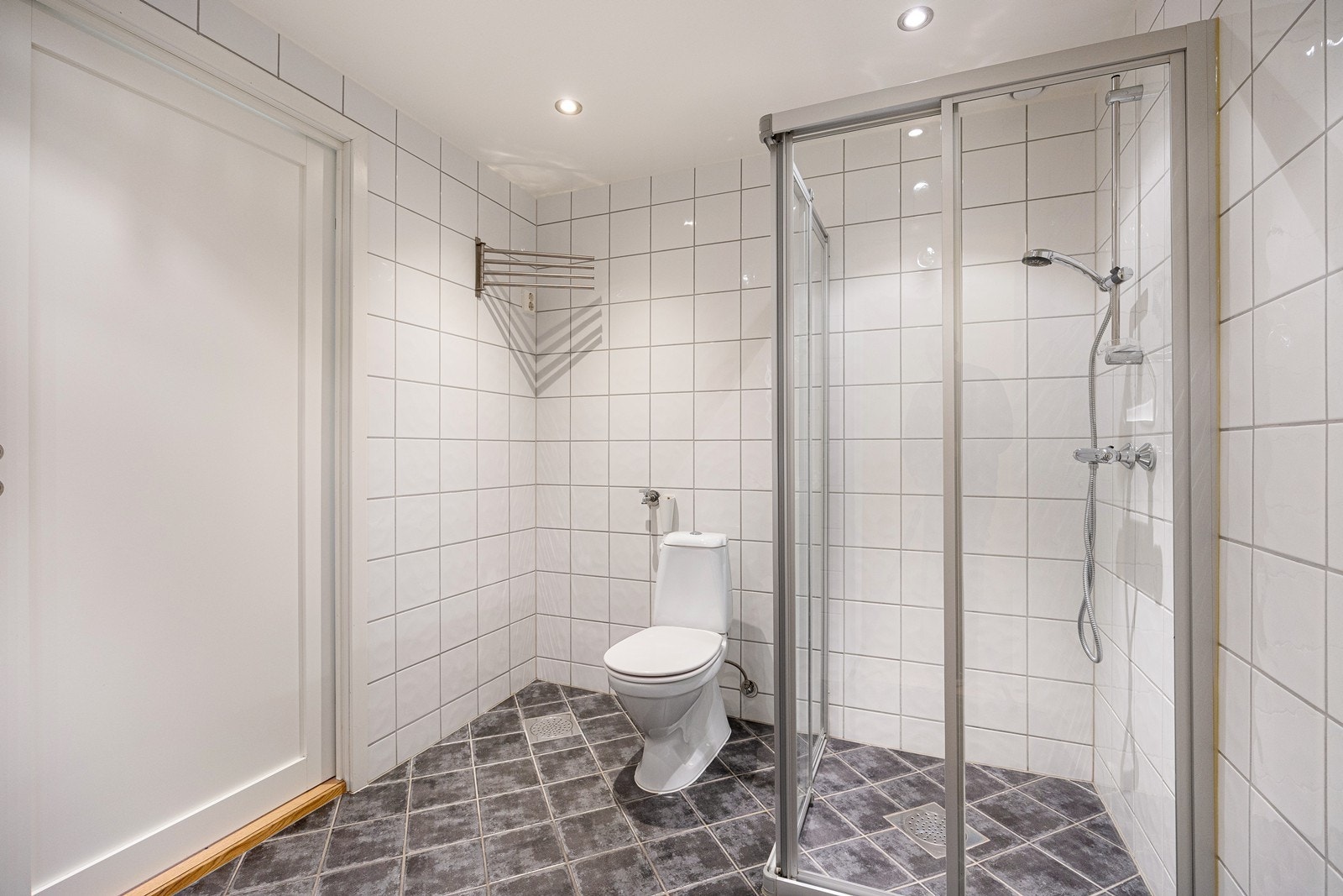 Videre har badet dusjhjørne med skyvedører, gulvmontert toalett og opplegg for vaskemaskin. Badet har adkomst både fra entréen og soverommet. Galleribilde