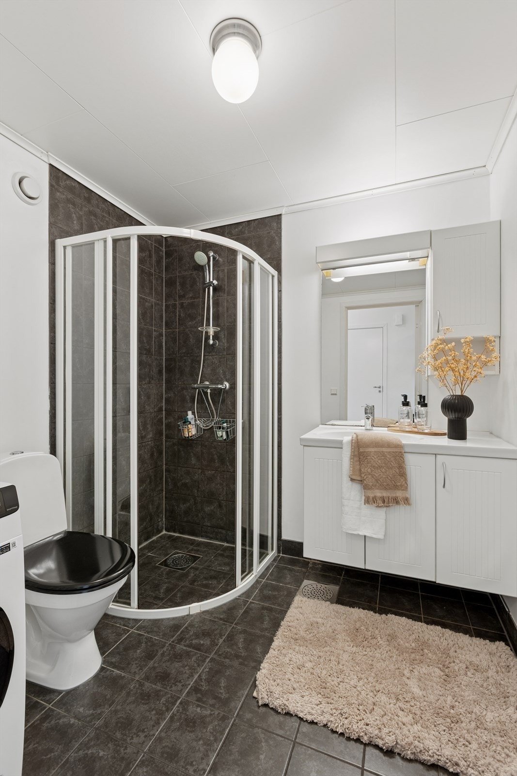 Badet har flislagt gulv, lys innredning, dusjsone og opplegg for vaskemaskin/tørk. Galleribilde